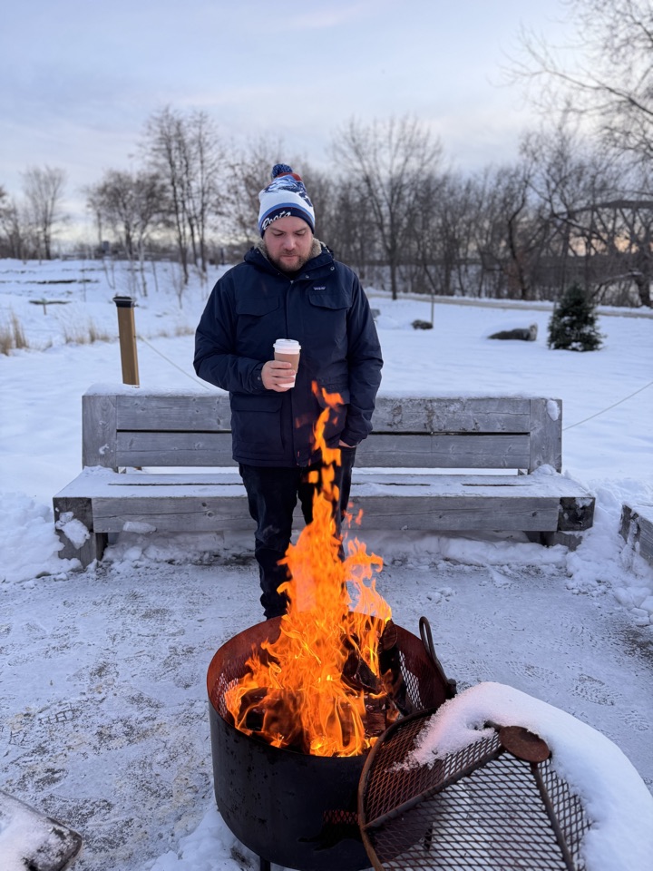 James enjoying a coffee by an outdoor fire in the snow